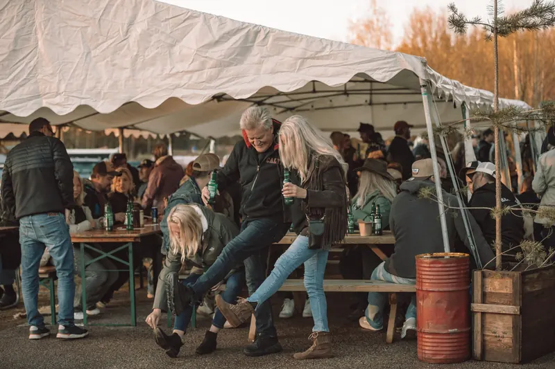 Ett par dansar med ölflaskor i händerna framför långborden under tältet på Backwoods 2026