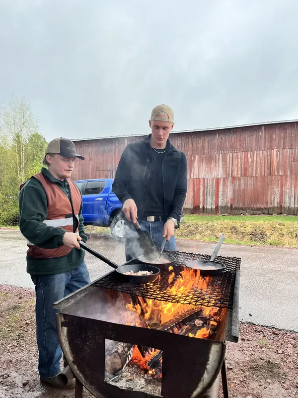 Två kockar steker mat i pannor över en öppen eldstad på Backwoods 2026