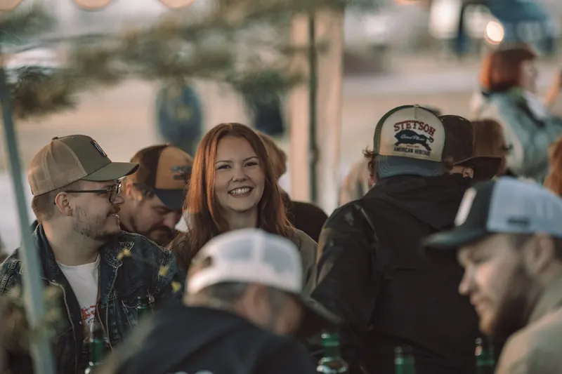 En leende besökare vid ett långbord bland folk i truckerkepsar under kvällen på Backwoods 2026