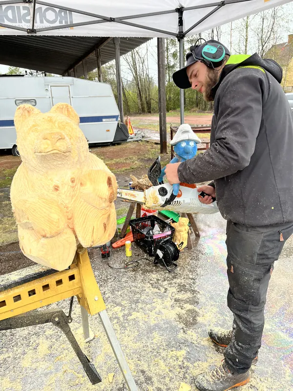 En motorsågskonstnär sågar fram en björn ur en trästock, med sågspån över hela marken, på Backwoods 2026