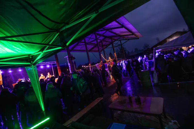 Publik under det lila upplysta sågverkstaket på natten, med scenen till vänster och ljusslingor över festivalområdet, på Backwoods 2026