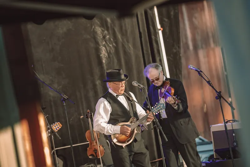Två medlemmar i Östen med Resten spelar mandolin och fiol på scenen i kvällssolen på Backwoods 2026