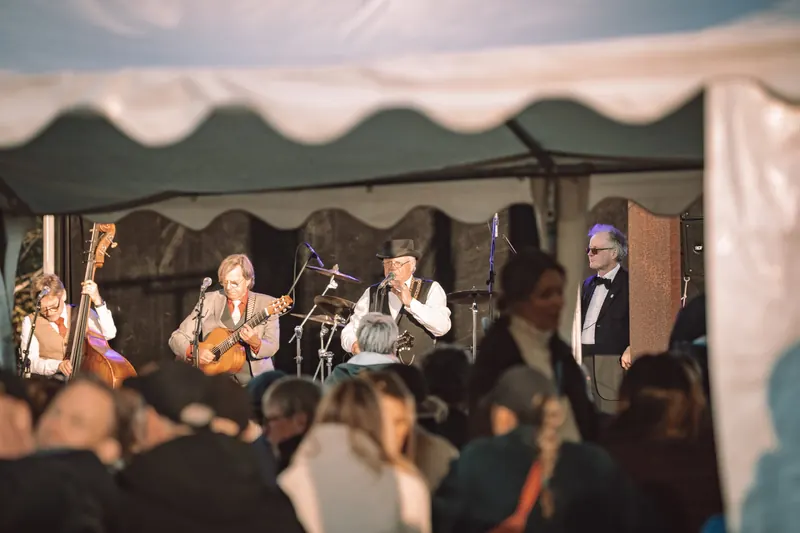 Östen med Resten spelar kontrabas och gitarr och sjunger på scenen under ett tält, med publiken i förgrunden, på Backwoods 2026